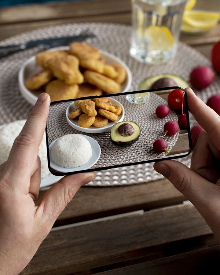 Cineva fotografiaza cu telefonul o farfurie cu nuggets de pui, orez si avocado — preparat cu alergenii si valorile nutritionale afisate in meniul digital QR